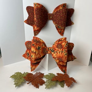 May include: Two large fabric bows with a sunflower and brown floral pattern. The bows are made of a soft, textured fabric and are perfect for adding a touch of fall decor to your home.