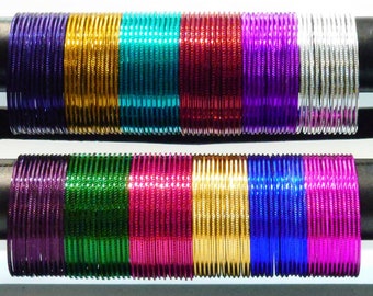May include: A set of colorful metal bangles in various shades of purple, green, gold, and silver. The bangles are stacked on a black stand.