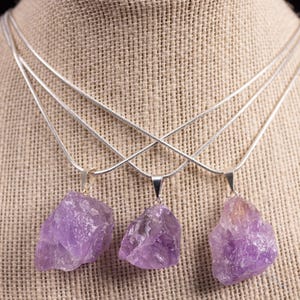 These pale lilac colored Amethyst crystal jewelry sets are raw crystal chunk pendants strung on a silver chain, with matching earrings on silver ear hooks.  
Crystals are nature-made therefore each one is unique in appearance.