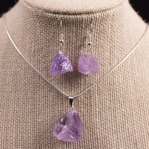 These pale lilac colored Amethyst crystal jewelry sets are raw crystal chunk pendants strung on a silver chain, with matching earrings on silver ear hooks.  
Crystals are nature-made therefore each one is unique in appearance.