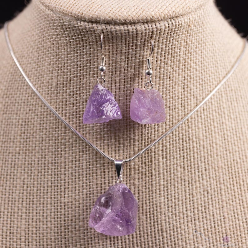 These pale lilac colored Amethyst crystal jewelry sets are raw crystal chunk pendants strung on a silver chain, with matching earrings on silver ear hooks.  
Crystals are nature-made therefore each one is unique in appearance.