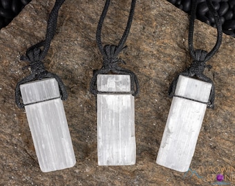 May include: Three rectangular selenite crystal pendants, each featuring a translucent white, fibrous texture. Every crystal is securely wrapped in a black cord necklace with a knotted design at the top, creating a uniform set of three individual necklaces.