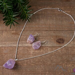 These pale lilac colored Amethyst crystal jewelry sets are raw crystal chunk pendants strung on a silver chain, with matching earrings on silver ear hooks.  
Crystals are nature-made therefore each one is unique in appearance.