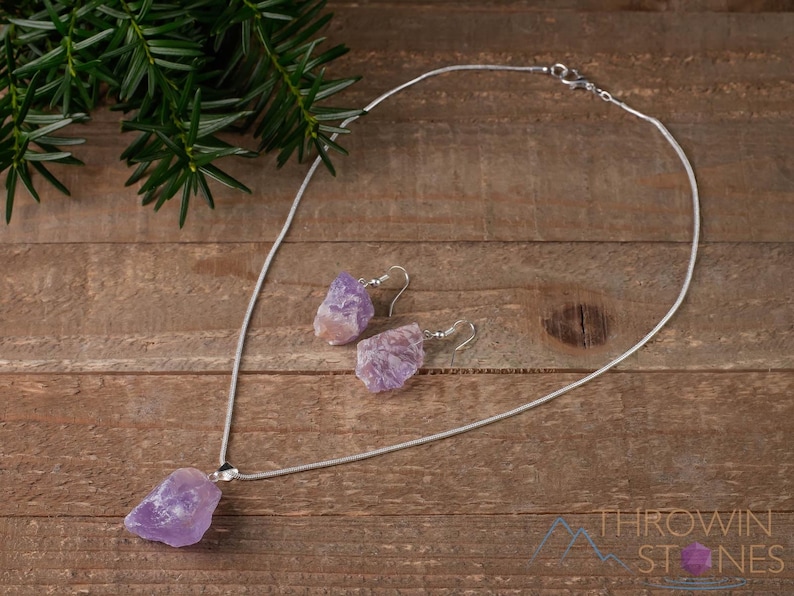 These pale lilac colored Amethyst crystal jewelry sets are raw crystal chunk pendants strung on a silver chain, with matching earrings on silver ear hooks.  
Crystals are nature-made therefore each one is unique in appearance.