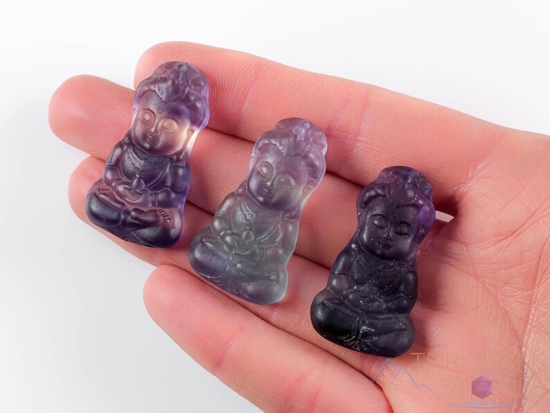 These rainbow Fluorite crystal pendants are carved in the shape of seated Buddha, with a small hole drilled.  Rainbow Fluorite is striated in sheer green, teal, and purple.
Crystals are nature-made therefore each one is unique in appearance.