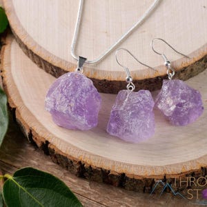 These pale lilac colored Amethyst crystal jewelry sets are raw crystal chunk pendants strung on a silver chain, with matching earrings on silver ear hooks.  
Crystals are nature-made therefore each one is unique in appearance.