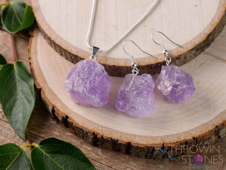 These pale lilac colored Amethyst crystal jewelry sets are raw crystal chunk pendants strung on a silver chain, with matching earrings on silver ear hooks.  
Crystals are nature-made therefore each one is unique in appearance.