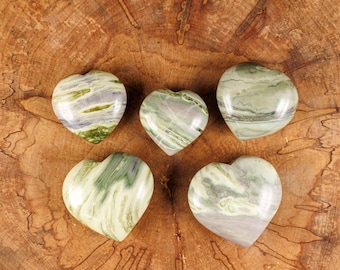May include: Five green and white heart-shaped stones with swirling patterns on a wooden surface.