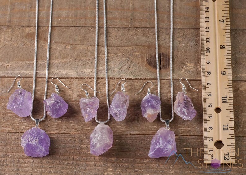 These pale lilac colored Amethyst crystal jewelry sets are raw crystal chunk pendants strung on a silver chain, with matching earrings on silver ear hooks.  
Crystals are nature-made therefore each one is unique in appearance.