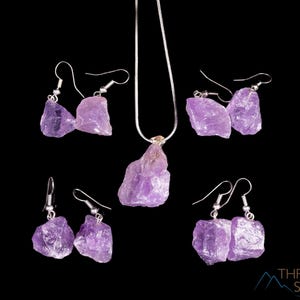 These pale lilac colored Amethyst crystal jewelry sets are raw crystal chunk pendants strung on a silver chain, with matching earrings on silver ear hooks.  
Crystals are nature-made therefore each one is unique in appearance.
