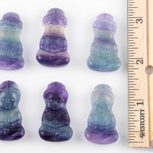 These rainbow Fluorite crystal pendants are carved in the shape of seated Buddha, with a small hole drilled.  Rainbow Fluorite is striated in sheer green, teal, and purple.
Crystals are nature-made therefore each one is unique in appearance.