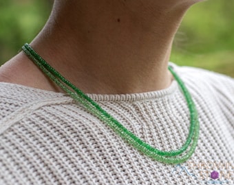 May include: A double strand necklace made of green gemstone beads. The beads are graduated in size, with the larger beads at the bottom of the necklace. The necklace is worn by a person with a white sweater.