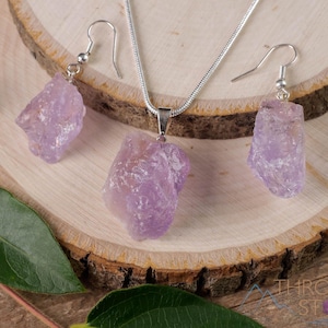 These pale lilac colored Amethyst crystal jewelry sets are raw crystal chunk pendants strung on a silver chain, with matching earrings on silver ear hooks.  
Crystals are nature-made therefore each one is unique in appearance.