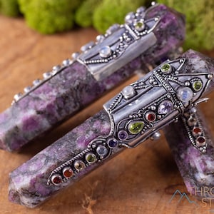 Può includere: Due bacchette di cristallo viola e argento con intricati dettagli in argento e pietre preziose colorate. Le bacchette sono posizionate su una superficie di legno.