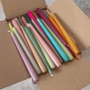 May include: A box filled with a variety of taper candles in assorted colors, including pink, green, yellow, orange, and blue.