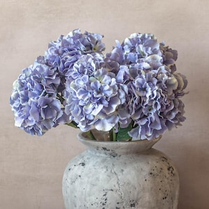 May include: A bouquet of lavender hydrangeas in a grey ceramic vase. The vase has a textured surface.