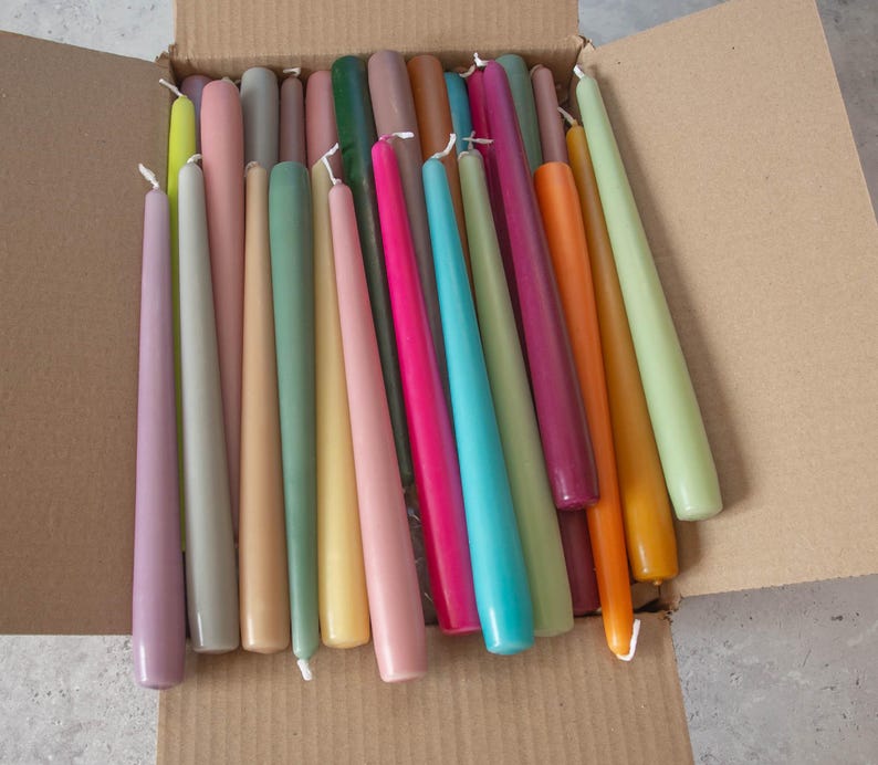 May include: A box filled with a variety of taper candles in different colors, including purple, gray, beige, green, yellow, pink, red, orange, blue, and brown.