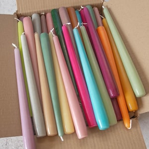 May include: A box filled with a variety of taper candles in pastel colors, including pink, green, yellow, and blue.