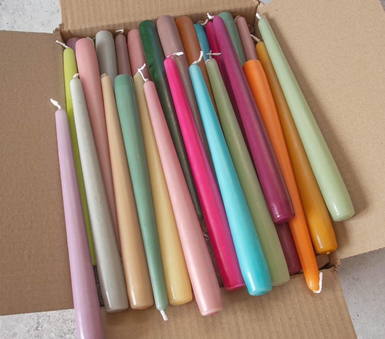 May include: A box filled with a variety of taper candles in pastel colors, including pink, green, yellow, and blue.