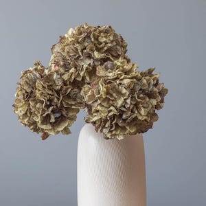 May include: Dried hydrangea flowers in a white ceramic vase with a textured surface.