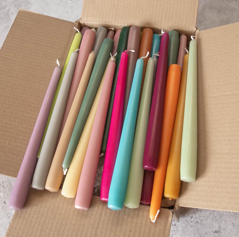 May include: A box filled with a variety of taper candles in different colors, including purple, green, blue, pink, orange, and yellow.