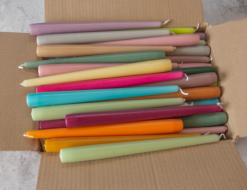 May include: A box filled with a variety of taper candles in assorted colors, including purple, pink, beige, yellow, green, blue, orange, and red.