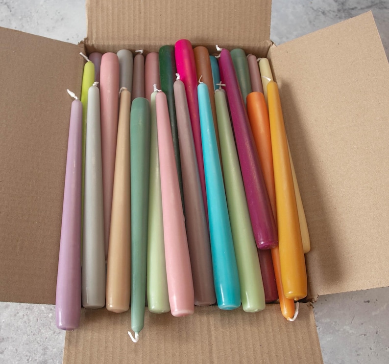 May include: A box filled with a variety of taper candles in different colors, including purple, gray, beige, green, light blue, pink, and orange.