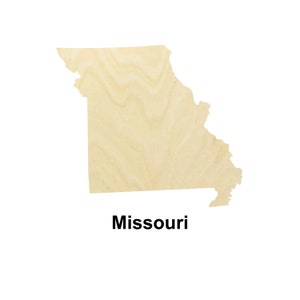 May include: A wooden cutout of the state of Missouri. The cutout is light brown and has a wood grain pattern. The word "Missouri" is printed below the cutout.