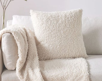 May include: A white fluffy throw blanket and pillow on a white couch. The throw blanket and pillow are made of a soft, plush material.
