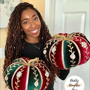 May include: Two decorative pumpkins made of velvet in alternating deep red and dark green segments. Each segment is separated by gold trim and embellished with gold vine embroidery and clear crystal floral accents. A gold stem tops each pumpkin.