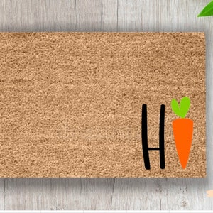 May include: A brown coir doormat with the word "Hi" in black lettering and a carrot with green leaves.