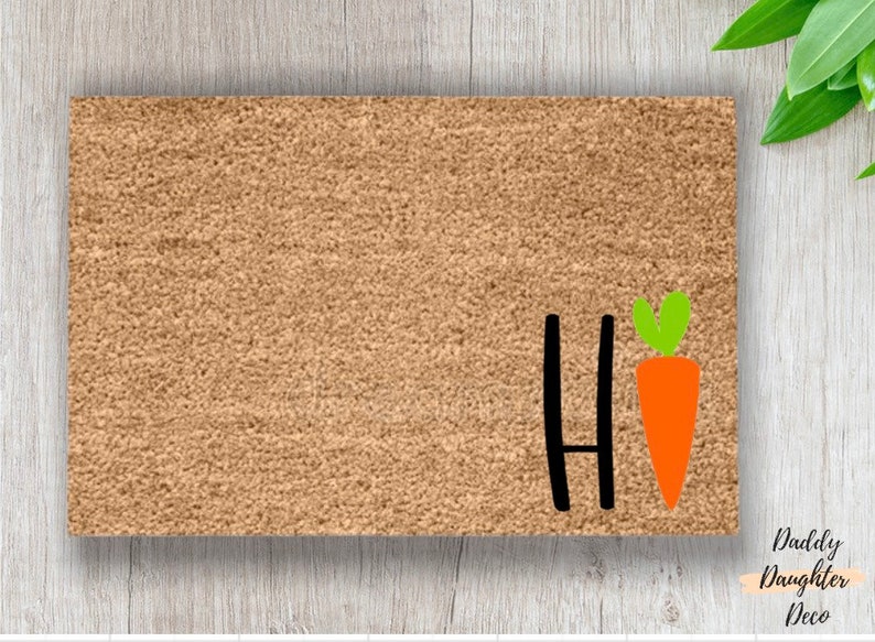 May include: A brown coir doormat with the word "Hi" in black lettering and a carrot with green leaves.