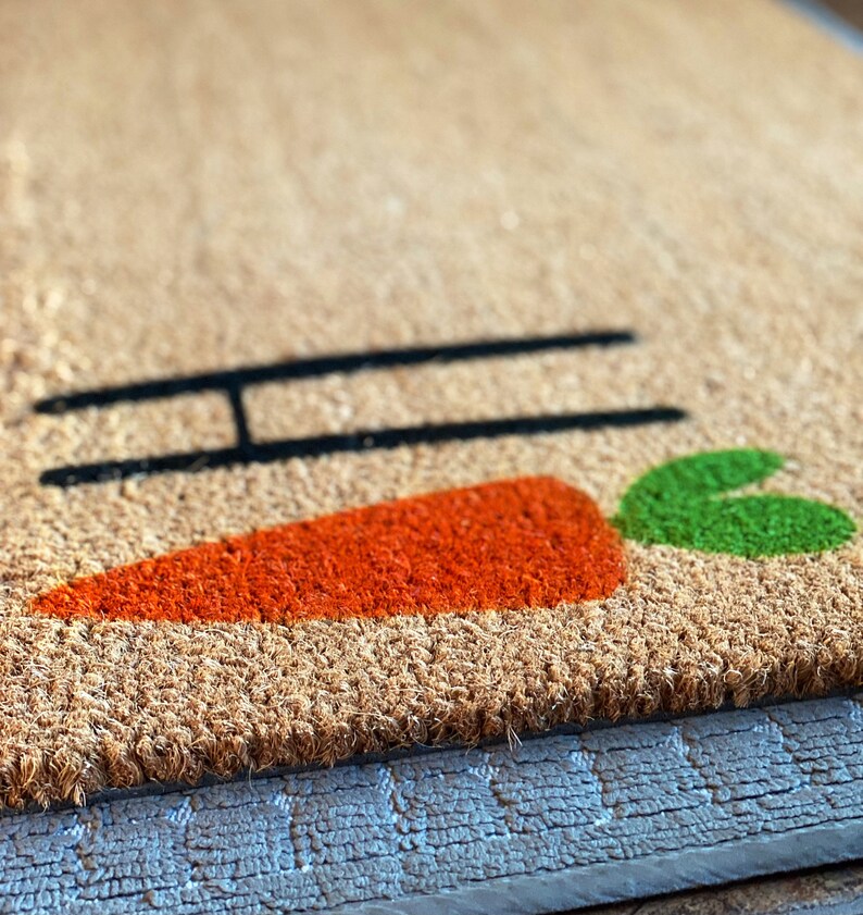 May include: A brown coir doormat with the word "Hi" and a carrot design in orange and green.