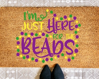 May include: A brown coir doormat with the text "I'm just here for the beads" in purple, yellow, and green lettering. The text is surrounded by a circle of purple, yellow, and green dots.