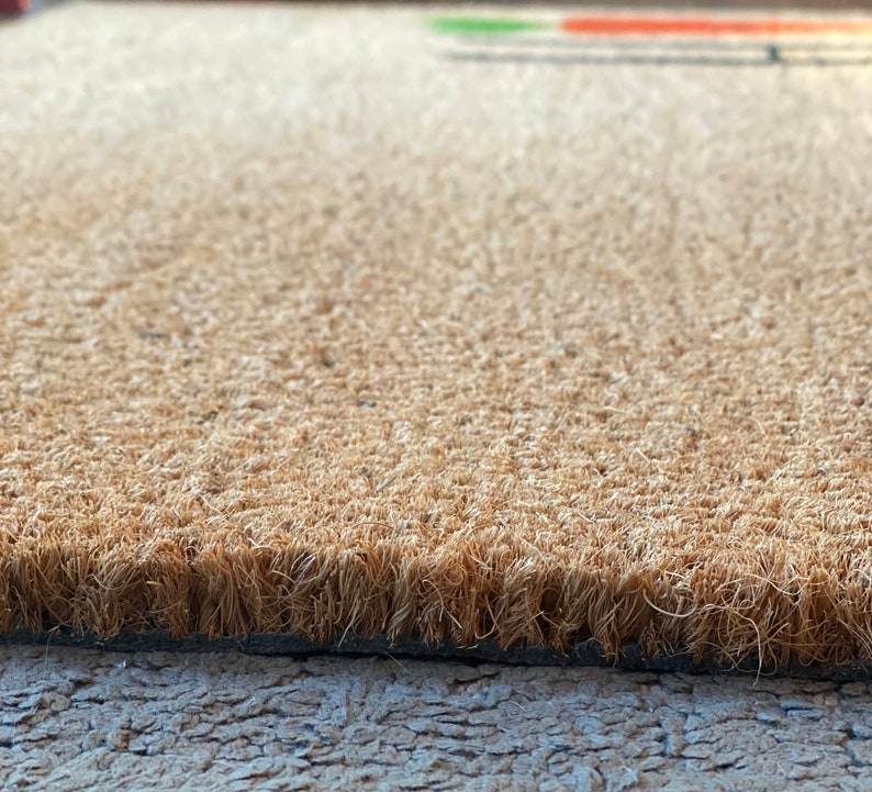 May include: Close-up of a brown coir doormat with a textured surface. The mat has a black backing.