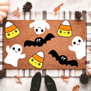 May include: A brown doormat with a white and black checkered border features various Halloween-themed illustrations, including ghosts, bats, and candy corn. The illustrations are in a cartoon style with smiling faces.