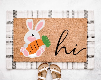 May include: A brown coir doormat with a white bunny holding a carrot and the word "hi" in black script.