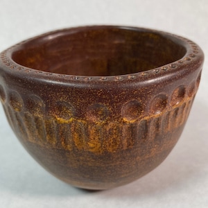 May include: A small, brown ceramic bowl with a textured, patterned design. The bowl has a slightly rounded bottom and a wide, open top.