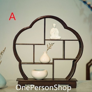 Può includere: Un ripiano in legno marrone scuro con un design a forma di nuvola. Il ripiano ha più scomparti ed è decorato con una statuetta in ceramica bianca e un piccolo vaso bianco con fiori secchi.