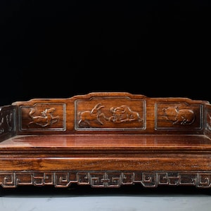 Peut inclure: Un petit banc rectangulaire en bois avec une finition brune polie. Le dossier présente trois panneaux sculptés représentant des animaux, tandis que la base est ornée d'un motif géométrique en grecque sur les bords avant et latéraux.