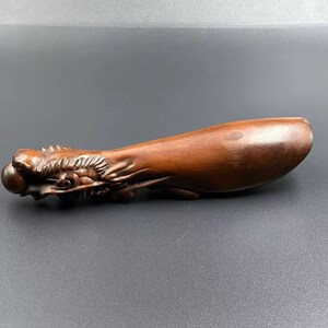 May include: A dark brown wooden carving of a dragon with a pearl in its mouth. The dragon is curled up in a long, thin shape.