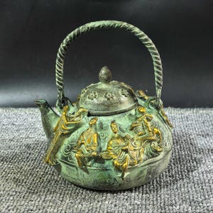 May include: A round, weathered green and gold metal teapot featuring a twisted handle and a lid adorned with floral patterns. The body of the teapot is decorated with raised, gold-toned relief figures of people in traditional attire, set against a textured, oxidised green surface.