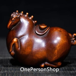 以下が含まれることがあります： 丸みを帯びたふっくらとした体と鞍を持つ馬の彫刻。濃い茶色の木でできており、滑らかで磨かれた仕上げが施されています。手彫りの木製の彫刻です。