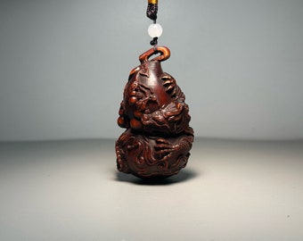 May include: A dark brown wooden pendant carved with a detailed dragon design. The pendant is shaped like a gourd and has a small loop at the top for hanging.