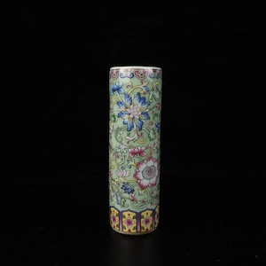Può includere: Un vaso cilindrico dipinto a mano con sfondo verde chiaro e motivi floreali. I fiori sono in tonalità blu, rosa e giallo. Il vaso ha una fascia decorativa in basso e in alto. Altezza circa 15 cm.