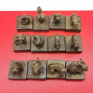 Peut inclure: Douze petites figurines en bois des animaux du zodiaque chinois, chacune sur une base carrée en bois. Les animaux sont sculptés en détail et peints en brun foncé. Les figurines sont disposées en rangée sur une surface rouge.