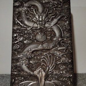 Puede incluir: Una caja de madera negra con una talla detallada de un dragón en un patrón de nubes. El dragón es de color plateado y tiene una perla en la boca.