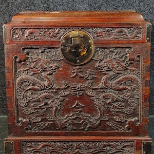 May include: A dark wood chest with intricate carvings of dragons and clouds. The chest has a brass lock and hinges. The text "天長地久" is carved into the front of the chest.