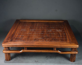 May include: A dark brown wooden table with a square top and a carved checkerboard pattern. The table has a simple, sturdy design with four legs.