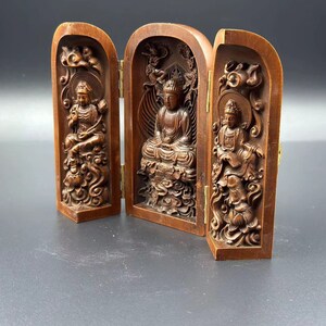 May include: A wooden folding shrine with three carved panels depicting Buddhist figures. The central panel shows a seated Buddha, while the side panels feature standing figures.